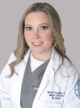 Person with long hair in a white lab coat over gray attire, against a plain background.